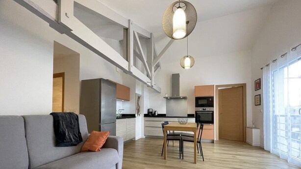A modern living room with a grey sofa, a wooden dining table, and a kitchen in the background. - TOUTOU - ANGLET - Gîte (ANGLET)