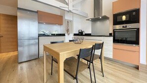 A modern kitchen with a wooden dining table, black chairs, a stainless steel refrigerator, a built-in oven, and a microwave. - TOUTOU - ANGLET - Gîte (ANGLET)