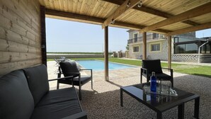 Une terrasse extérieure avec une piscine, un espace salon couvert et une vue sur une maison en arrière-plan.