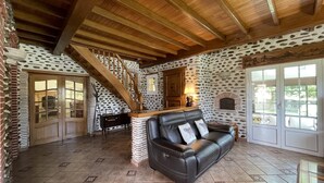 Un vaste espace de vie doté d’un plafond en bois, d’un canapé en cuir noir, d’un escalier et d’un mur dont le motif rappelle la pierre.
