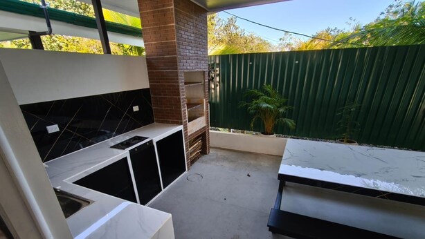 A patio area with a brick fireplace, a white countertop, and a green fence in the background.