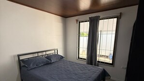 A bedroom with a single bed, a window with curtains, and a ceiling light.