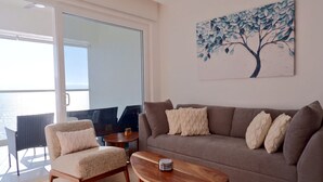 Una sala de estar con sofá, sillón y mesa de centro. Hay un cuadro de un árbol en la pared.