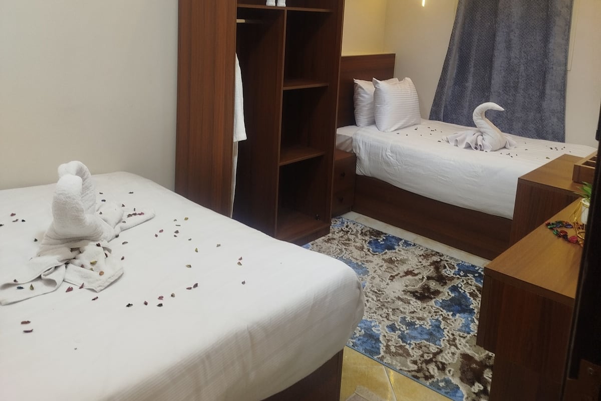 A hotel room with two beds, a wardrobe, a desk, and a patterned rug.