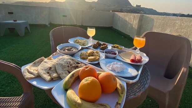 A table set with breakfast items and a glass of orange juice on a terrace with a view of pyramids and the sun setting. - Isis pyramids view inn  (Giza)