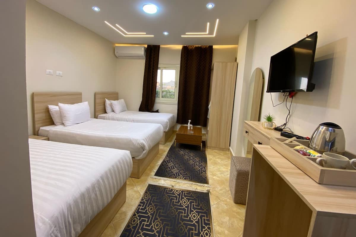 A hotel room with three beds, a TV, a desk with a mirror, and a window with curtains.