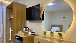 A modern hotel room with a wooden wardrobe, a built-in TV, a bedside table with plants, and a mirror with a circular light. - Isis pyramids view inn  (Giza)