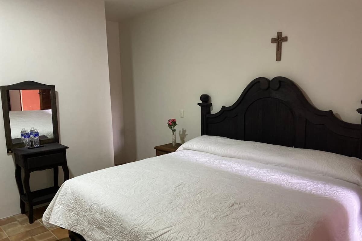 A bedroom with a bed, a nightstand, a mirror, and a wall-mounted cross.
