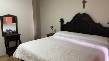 Un dormitorio con cama, mesita de noche, espejo y una cruz colgada en la pared.