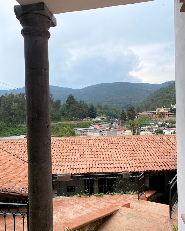 A balcony with a tiled roof overlooking a mountainous landscape and a village below. - Posada Conchita (Tlalpujahua)
