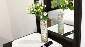A mirror reflecting a bed with a floral headboard, a remote control on a textured mat, and a vase with flowers on a bedside table. - Posada Conchita  (Tlalpujahua)