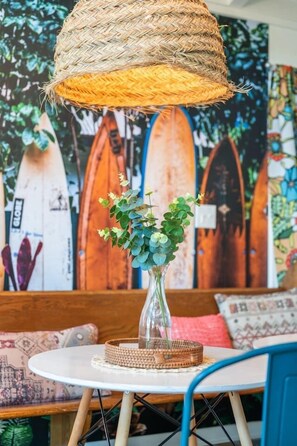 A round table with a woven basket centerpiece, a hanging woven lamp, and a wall with surfboard art.