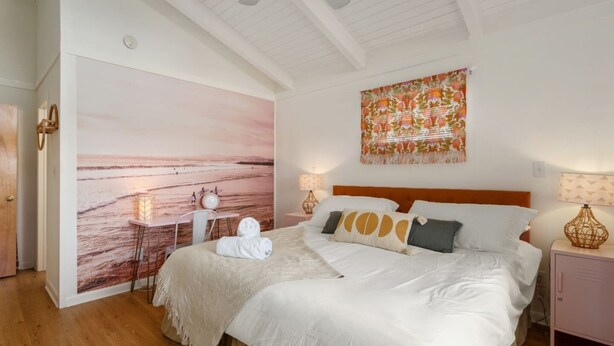 A bedroom with a bed, bedside tables, a wall mural, and a ceiling fan. - Hygge By The Sea: Beachfront Retreat (Avon)