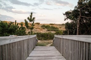 A wooden boardwalk leading to a natural landscape with dunes and sparse vegetation.