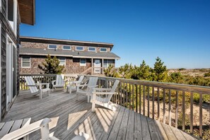 A wooden deck with white chairs, a building with stone facade, and a clear view of the beach. - Hygge By The Sea | Beachfront & Pet Friendly (Avon)