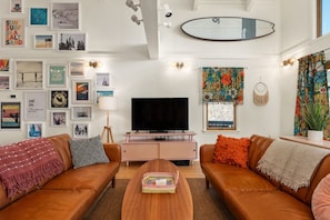 A living room with a TV, two sofas, a coffee table, and a surfboard decoration.