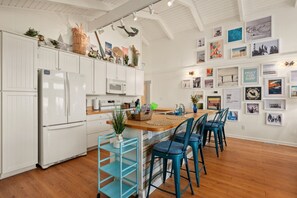 A modern kitchen with white cabinetry, a central island with bar stools, and a wall adorned with framed photographs.