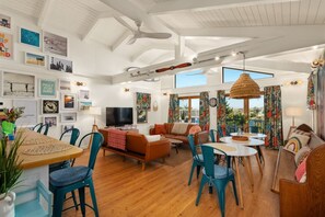 A spacious living room with a large TV, wooden flooring, and a ceiling fan. - Hygge By The Sea | Beachfront & Pet Friendly (Avon)