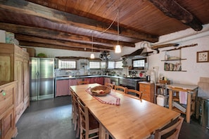 A rustic kitchen with wooden beams, a wooden dining table, and a refrigerator. - Apartment 'Le Fratte' with Mountain View, Private Garden and Wi-Fi (Pertica Alta)