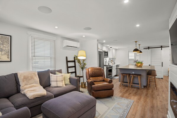 Una sala moderna con un sofá, un sillón y un comedor con taburetes.
