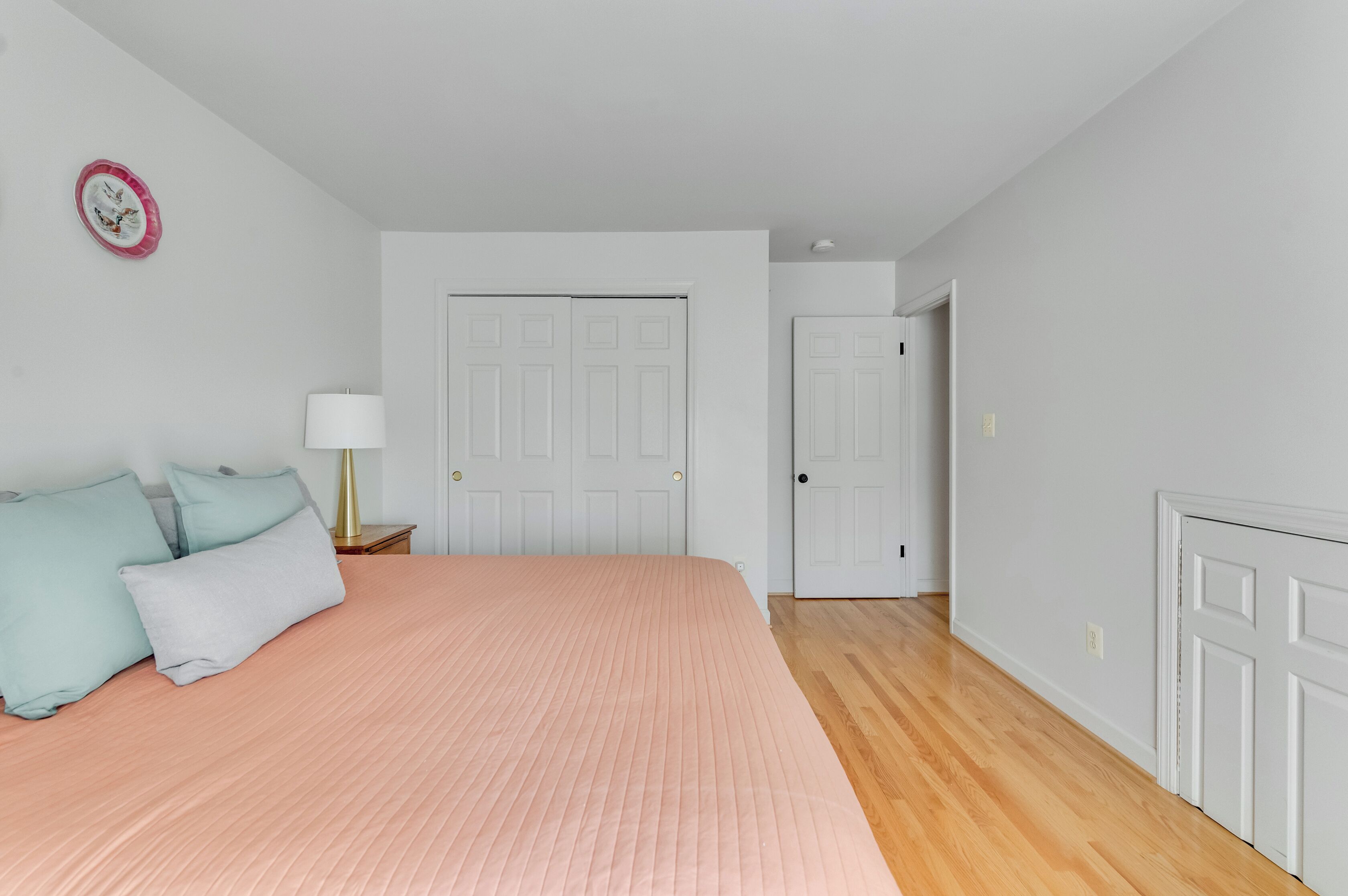 Une chambre à coucher avec un lit, des oreillers, une table de chevet, une lampe et une porte.
