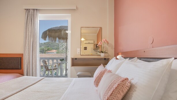 Et hotelværelse med seng, balkon med udsigt, et spejl og et lille bord med en vase.