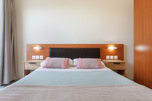 Een net opgemaakt bed met hoofdbord, twee nachtkastjes en een bijzettafeltje met lampen.