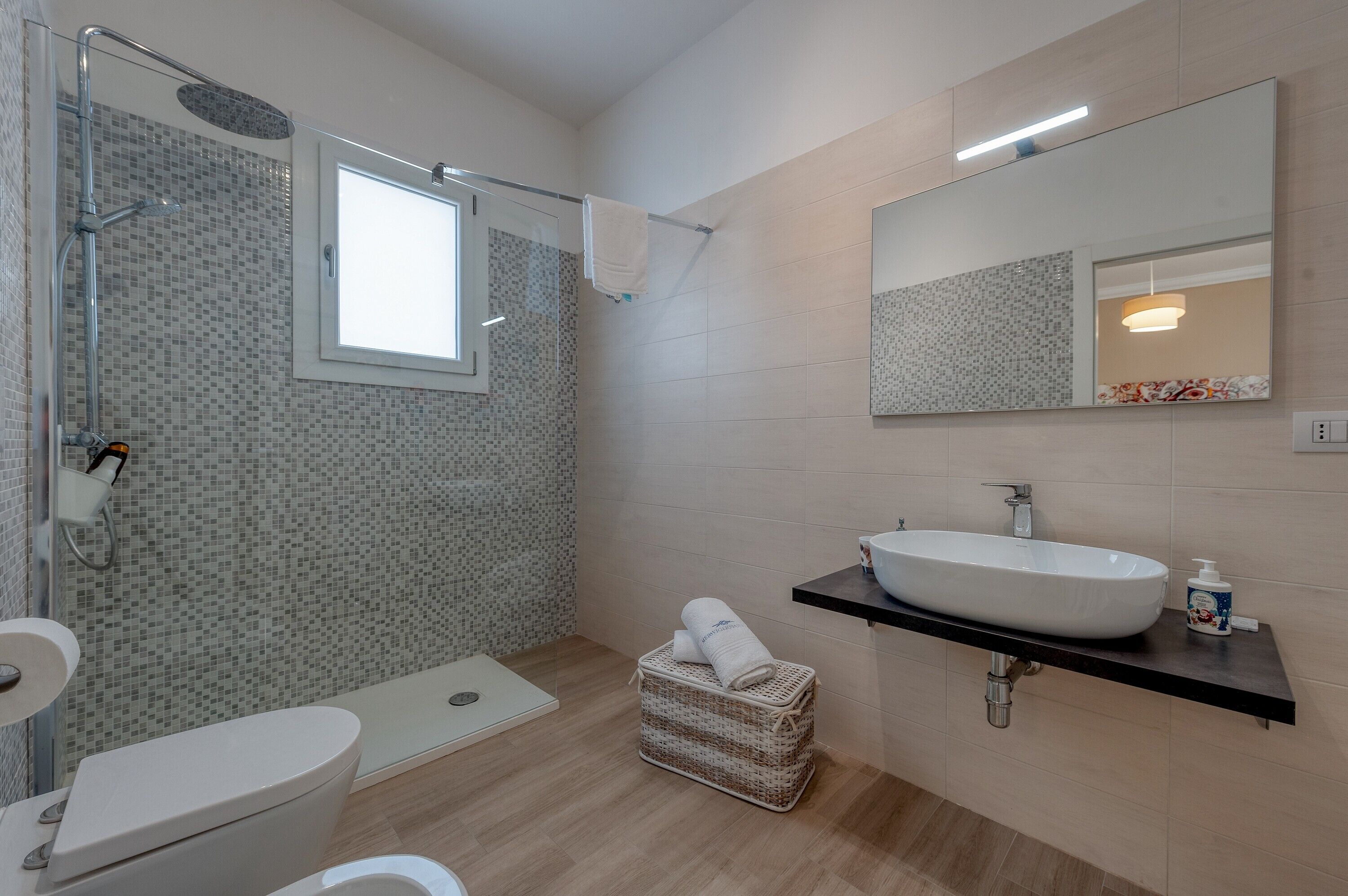 Une salle de bain moderne avec une douche à l’italienne en verre, un lavabo blanc et un grand miroir.