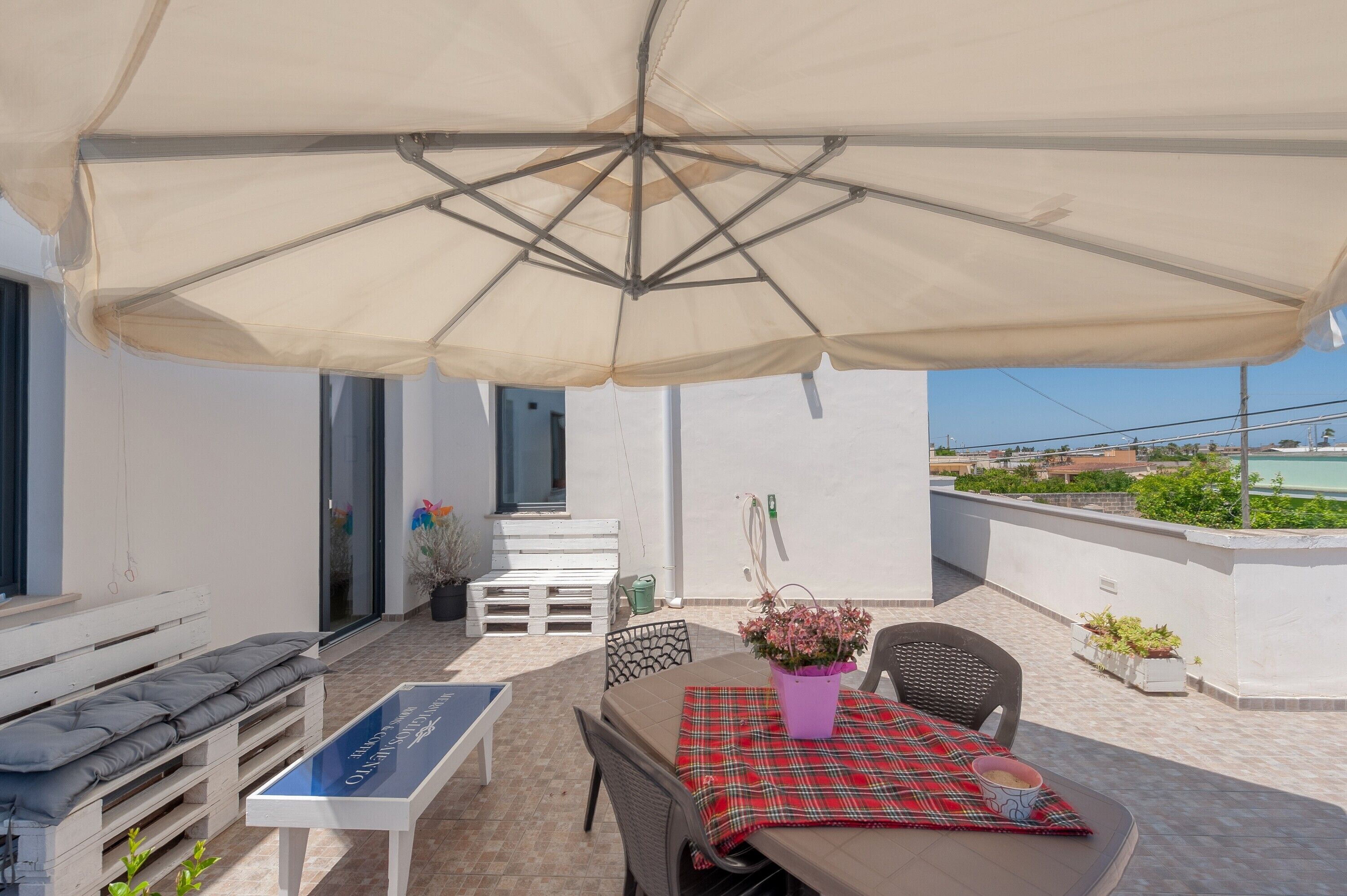 Eine Terrassengruppe mit Tisch, Stühlen, einer Bank und einem großen Sonnenschirm.
