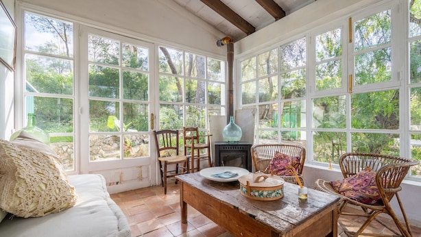Una habitación con ventanas amplias, chimenea, muebles de mimbre y una mesa de madera rústica.