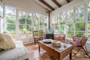 A room with large windows, a fireplace, wicker furniture, and a rustic wooden table.