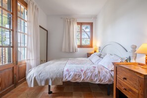 A bedroom with a bed, a nightstand, a lamp, a window with curtains, and a door.