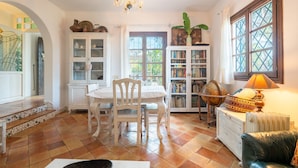 Una habitación con una mesa de comedor, sillas, una estantería, un radiador y una ventana con cortinas.