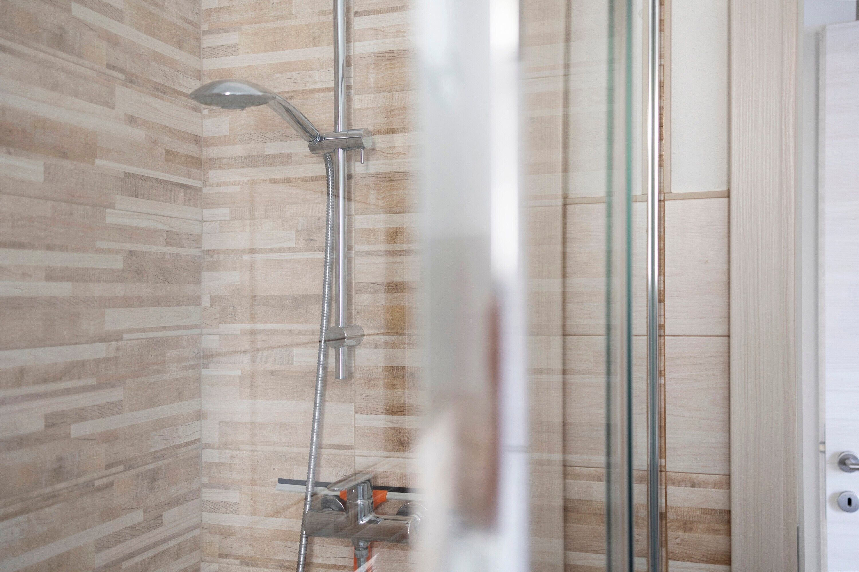 A shower with a glass door, a wooden wall, and a metal showerhead.