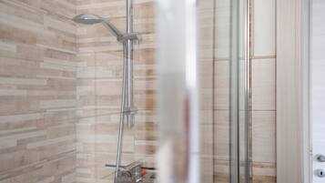 A shower with a glass door, a wooden wall, and a metal showerhead.