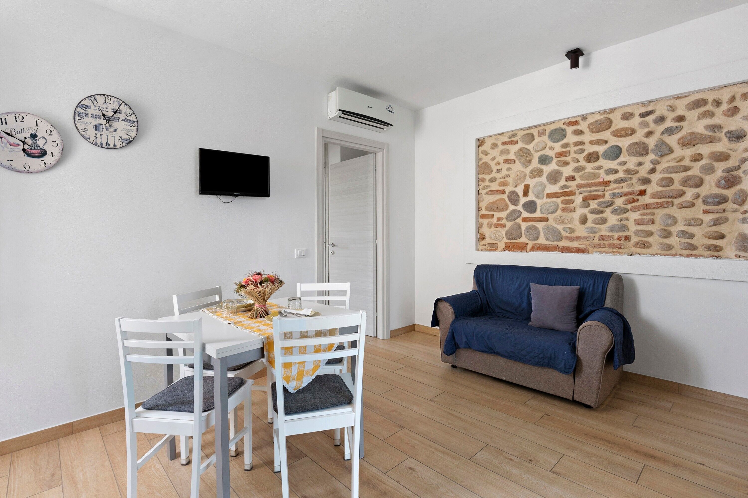 Ein Zimmer mit Esstisch, Stühlen, einer Couch, einer Steinwand, einem Fernseher und einer Klimaanlage.