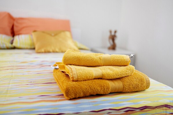 A neatly folded stack of yellow towels on a bed with a colorful striped bedspread.