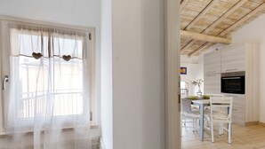A kitchen with a modern design, a dining area with white furniture, and a large window with sheer curtains.