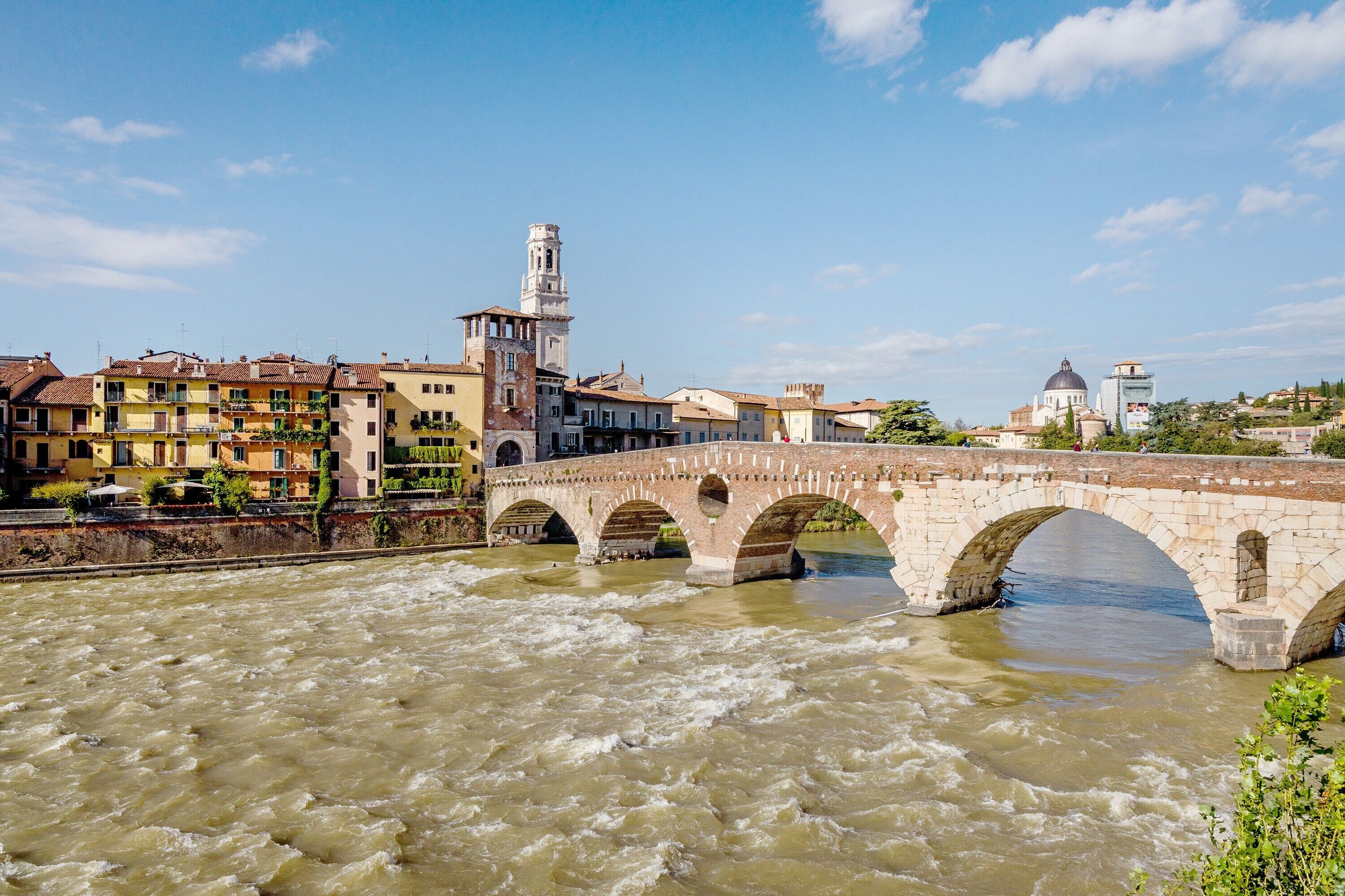 A stone bridge over a river with buildings and a tower in the background.