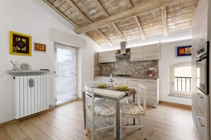 Uma cozinha com vigas de madeira no teto, armários brancos, uma mesa de jantar com cadeiras e uma janela com vista.