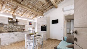 A modern kitchen with wooden beams, a dining area with a table and chairs, and a bedroom with a bed and a door.
