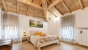A bedroom with a wooden ceiling, a bed with a patterned bedspread, a nightstand, a lamp, and a painting on the wall.