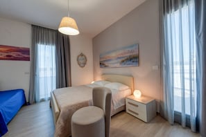 Quarto de hotel com cama, mesa de cabeceira, luminária, cadeira e uma obra de arte na parede.