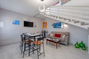 Uma sala de estar moderna com área de jantar, um sofá, uma mesa de centro e uma escada com corrimão.