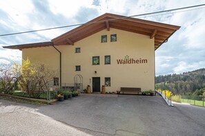 Ein Gebäude mit der Aufschrift 'Waldheim' an der Fassade, einem überdachten Eingang und Blick auf eine hügelige Landschaft.