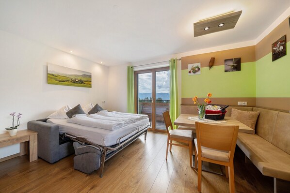 Une chambre moderne avec un lit, un canapé, une table à manger et une vue sur l’extérieur grâce à une grande fenêtre.