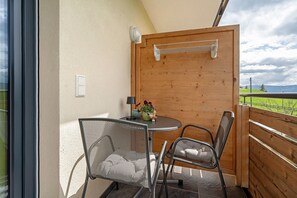 Ein Balkon mit Tisch und zwei Stühlen, eine Holzvertäfelung und Blick auf eine grüne Landschaft.