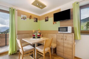 Ein Eckzimmer mit Tisch, Stühlen, einer Mikrowelle und einem Fernseher an der Wand.