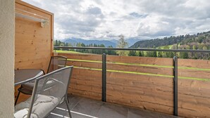 Un balcón con mesa y sillas, una valla de madera y vistas a montañas y árboles.