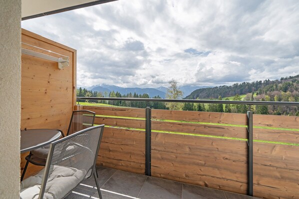 Een balkon met een tafel en stoelen, een houten hek en uitzicht op bergen en bomen.